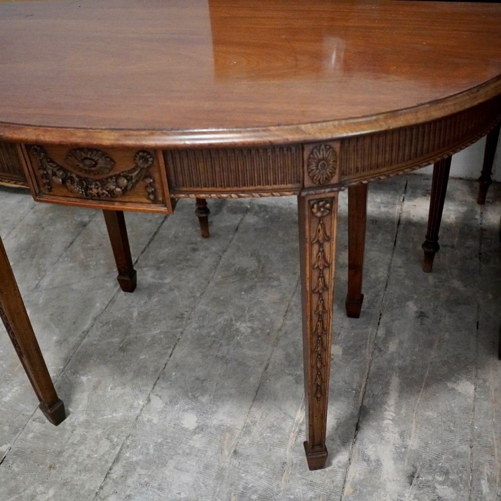 A long late George III mahogany extending dining table with D-shaped end sections, fluted friezes, carved paterae, and square tapered legs. View III