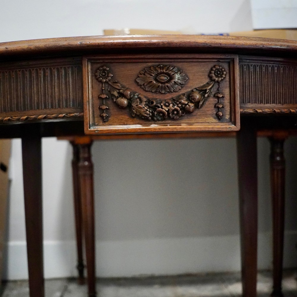 A long late George III mahogany extending dining table with D-shaped end sections, fluted friezes, carved paterae, and square tapered legs. View IV