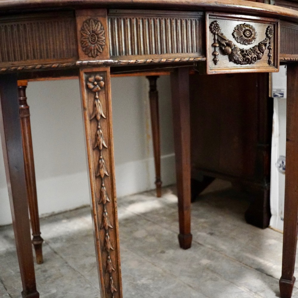 A long late George III mahogany extending dining table with D-shaped end sections, fluted friezes, carved paterae, and square tapered legs. View V
