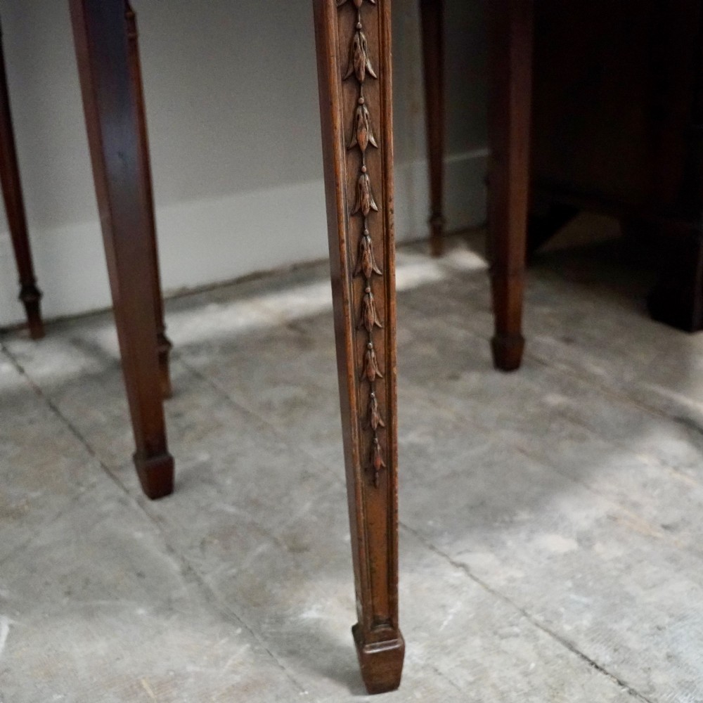 A long late George III mahogany extending dining table with D-shaped end sections, fluted friezes, carved paterae, and square tapered legs. View VI