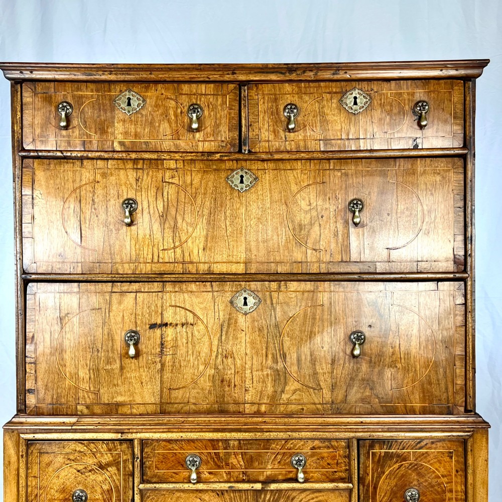 An early 18th-century Queen Anne walnut chest on stand featuring crossbanded drawers, brass teardrop handles, and cabriole legs. View II