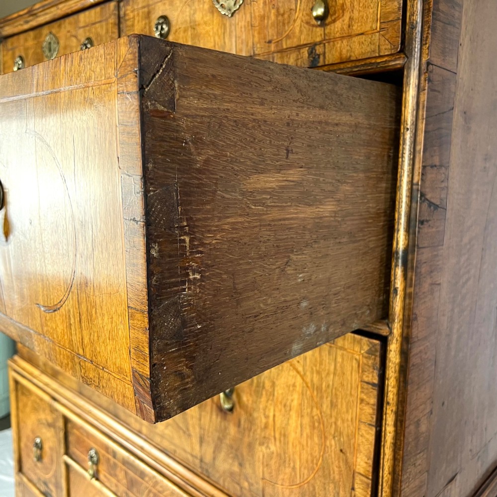 An early 18th-century Queen Anne walnut chest on stand featuring crossbanded drawers, brass teardrop handles, and cabriole legs. View VII