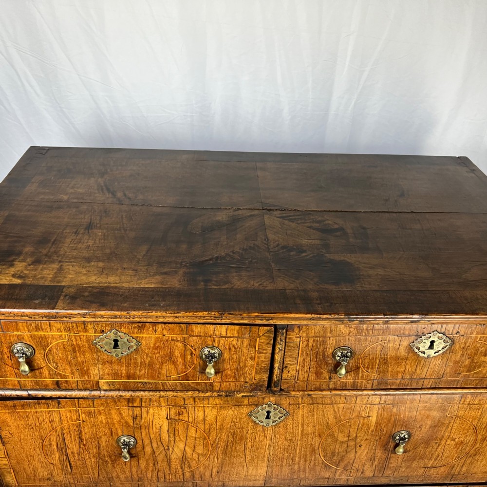 An early 18th-century Queen Anne walnut chest on stand featuring crossbanded drawers, brass teardrop handles, and cabriole legs. View X