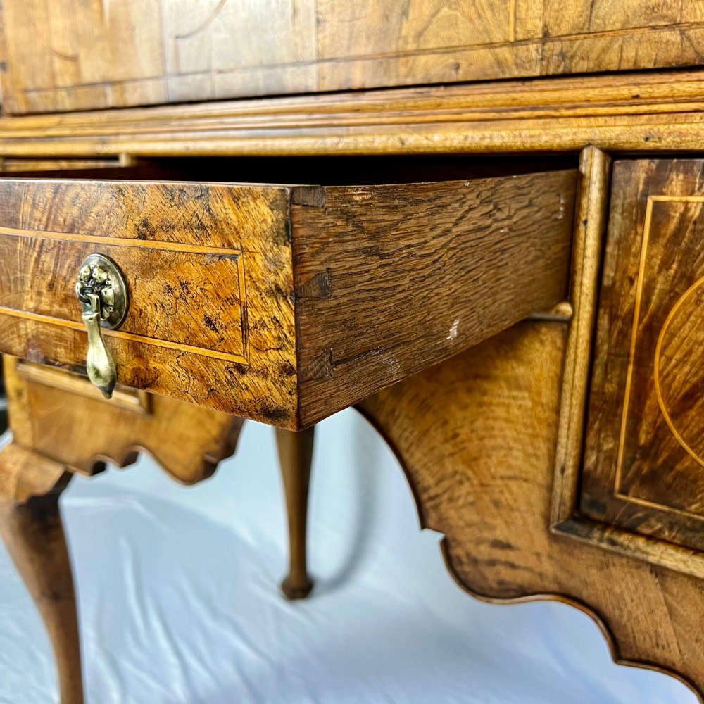 An early 18th-century Queen Anne walnut chest on stand featuring crossbanded drawers, brass teardrop handles, and cabriole legs. View XI