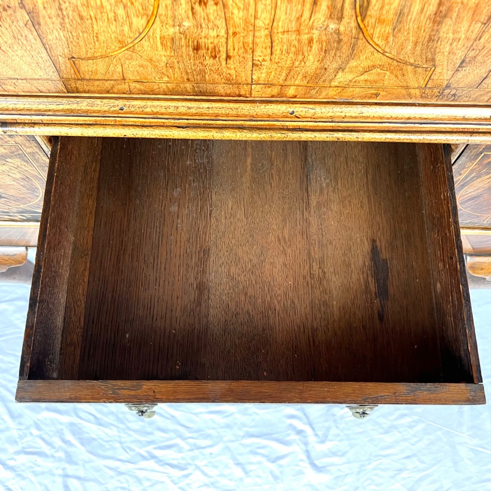 An early 18th-century Queen Anne walnut chest on stand featuring crossbanded drawers, brass teardrop handles, and cabriole legs. View XIII