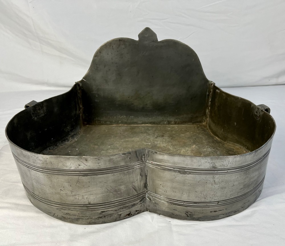 An 18th-century dark chestnut wood lavabo cabinet featuring a carved backboard mounted with a pewter cistern above a matching pewter basin. View V