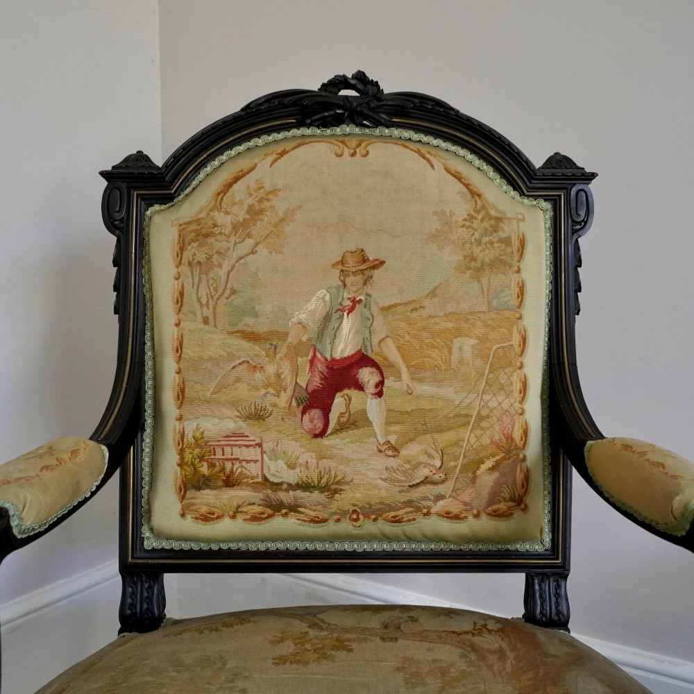 A pair of ebonised beech Louis XVI Revival salon armchairs featuring carved frames, fluted legs, padded armrests, and tapestry upholstery, accompanied by matching footstools. View II