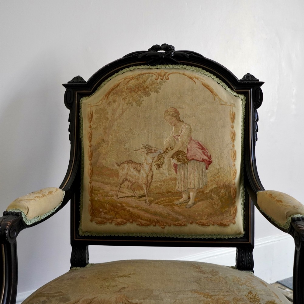A pair of ebonised beech Louis XVI Revival salon armchairs featuring carved frames, fluted legs, padded armrests, and tapestry upholstery, accompanied by matching footstools. View III