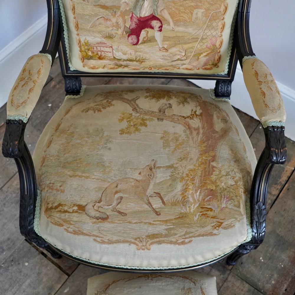 A pair of ebonised beech Louis XVI Revival salon armchairs featuring carved frames, fluted legs, padded armrests, and tapestry upholstery, accompanied by matching footstools. View IV