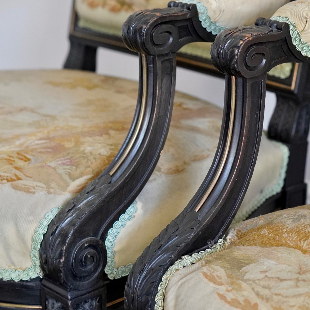 A pair of ebonised beech Louis XVI Revival salon armchairs featuring carved frames, fluted legs, padded armrests, and tapestry upholstery, accompanied by matching footstools. View XI