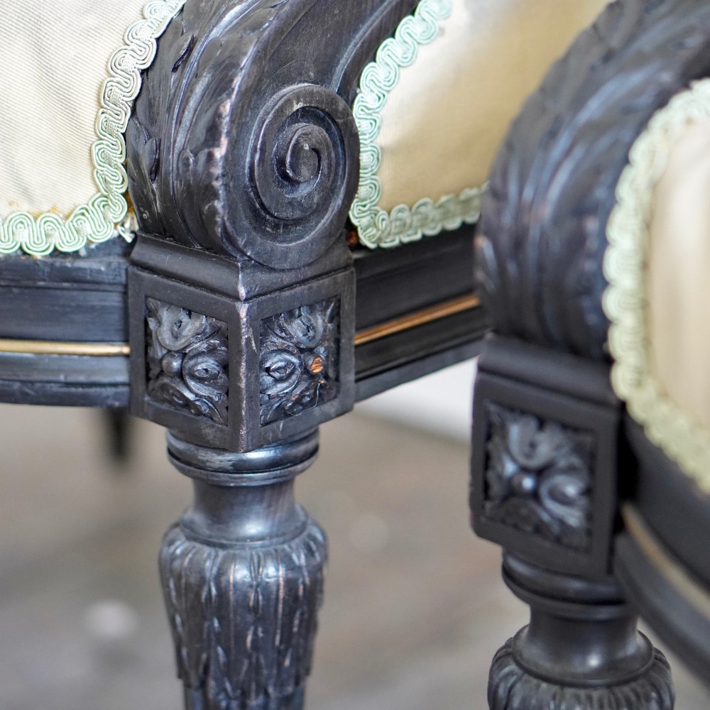 A pair of ebonised beech Louis XVI Revival salon armchairs featuring carved frames, fluted legs, padded armrests, and tapestry upholstery, accompanied by matching footstools. View XII