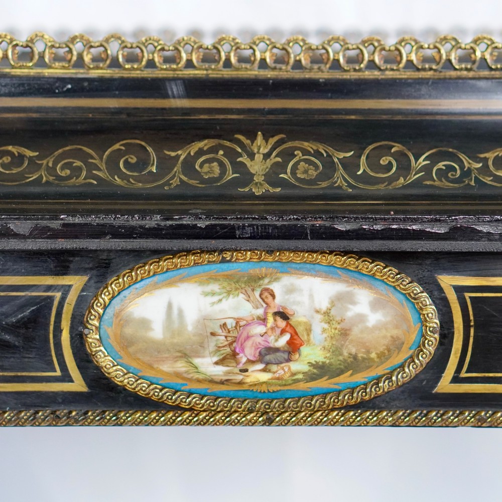 A French Napoleon III ebonised jardiniere stand featuring gilt highlights, inset painted porcelain plaques, a pierced brass gallery top, turned legs, and an arched lower stretcher. View II