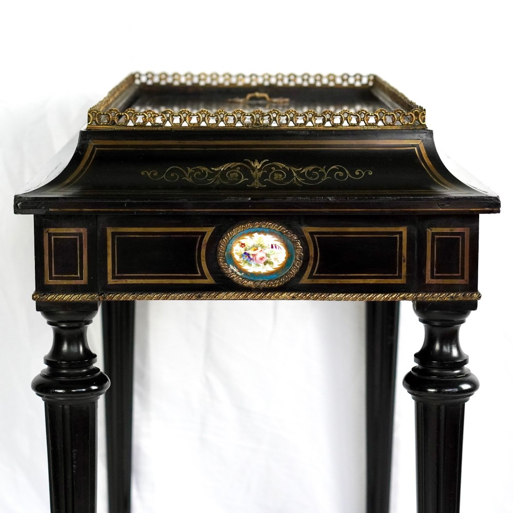 A French Napoleon III ebonised jardiniere stand featuring gilt highlights, inset painted porcelain plaques, a pierced brass gallery top, turned legs, and an arched lower stretcher. View VIII