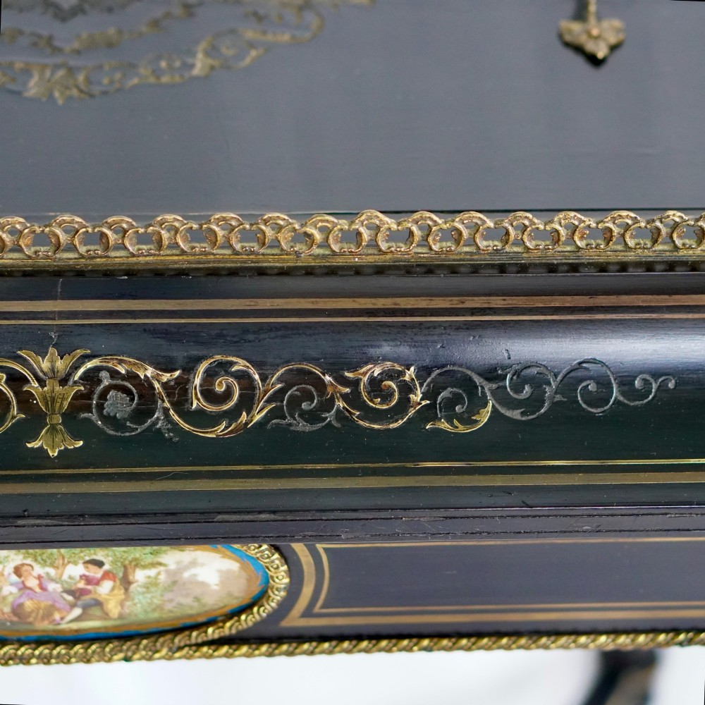 A French Napoleon III ebonised jardiniere stand featuring gilt highlights, inset painted porcelain plaques, a pierced brass gallery top, turned legs, and an arched lower stretcher. View IX