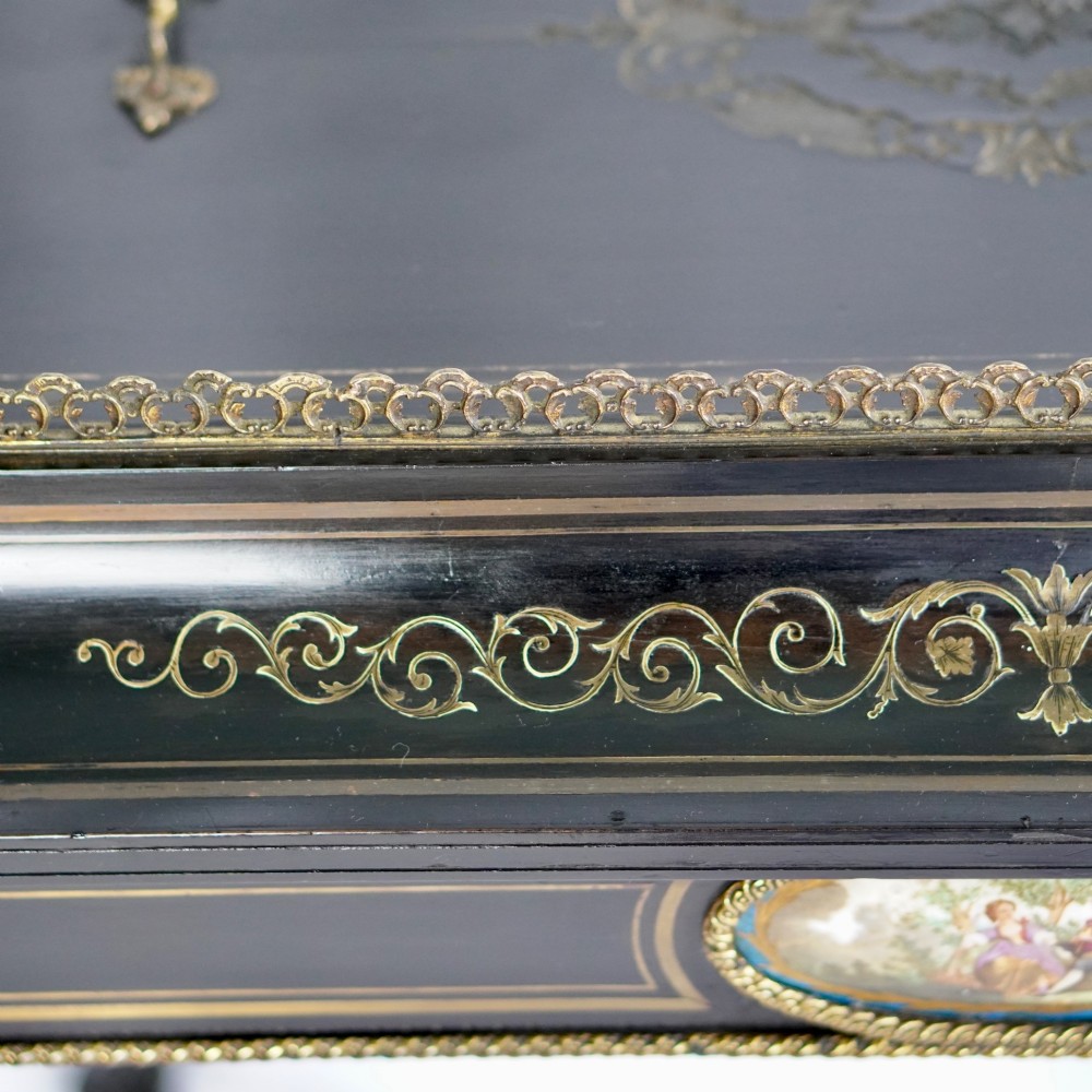 A French Napoleon III ebonised jardiniere stand featuring gilt highlights, inset painted porcelain plaques, a pierced brass gallery top, turned legs, and an arched lower stretcher. View X