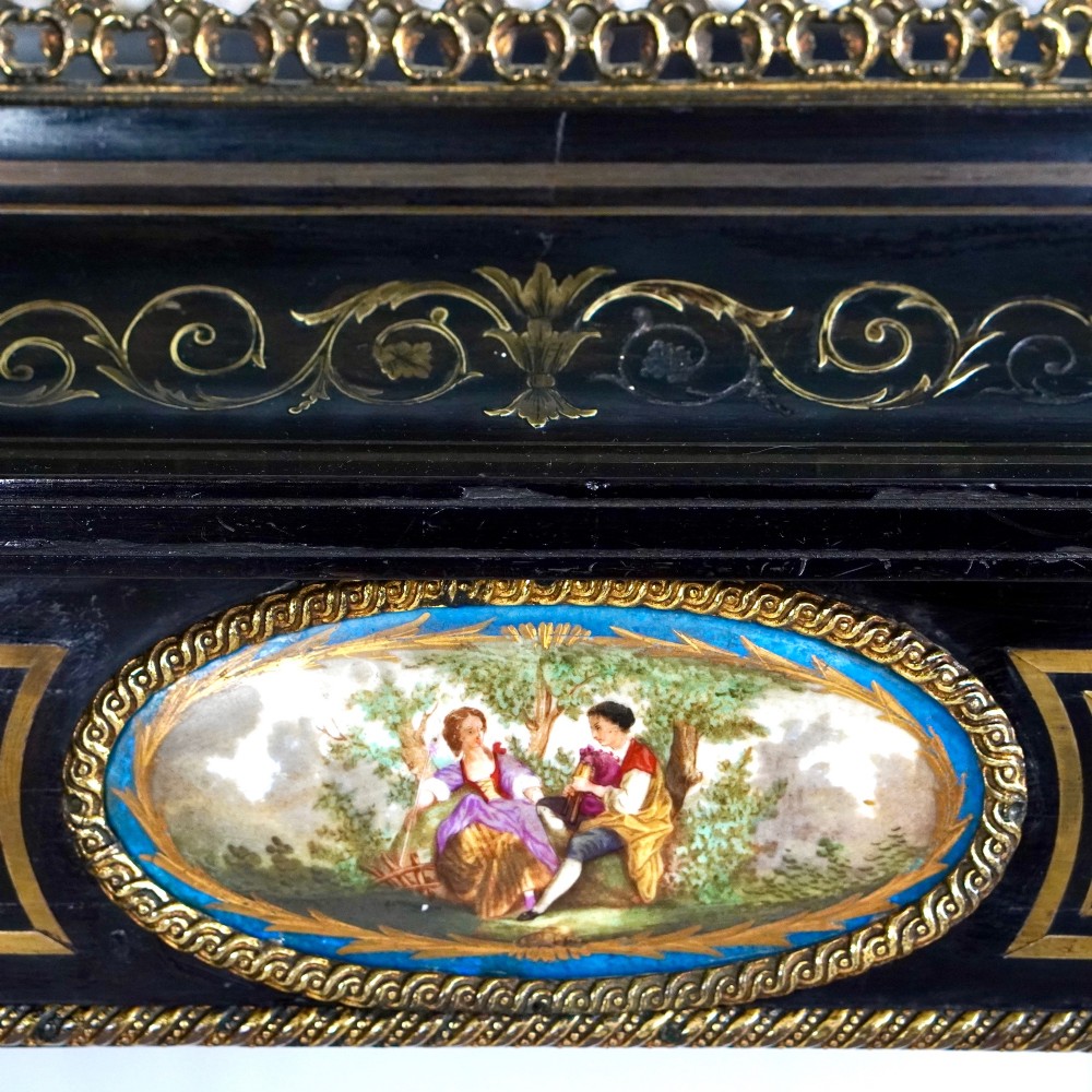 A French Napoleon III ebonised jardiniere stand featuring gilt highlights, inset painted porcelain plaques, a pierced brass gallery top, turned legs, and an arched lower stretcher. View XI