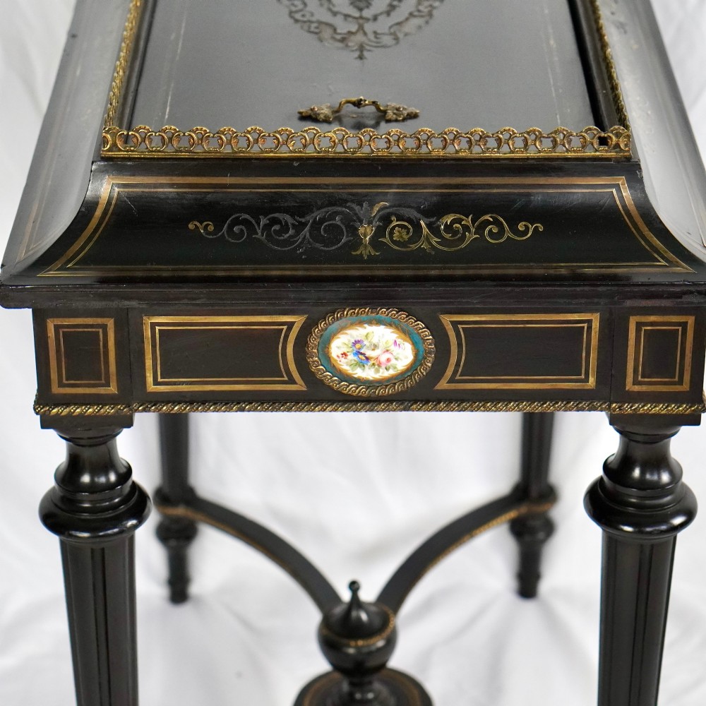 A French Napoleon III ebonised jardiniere stand featuring gilt highlights, inset painted porcelain plaques, a pierced brass gallery top, turned legs, and an arched lower stretcher. View XIII