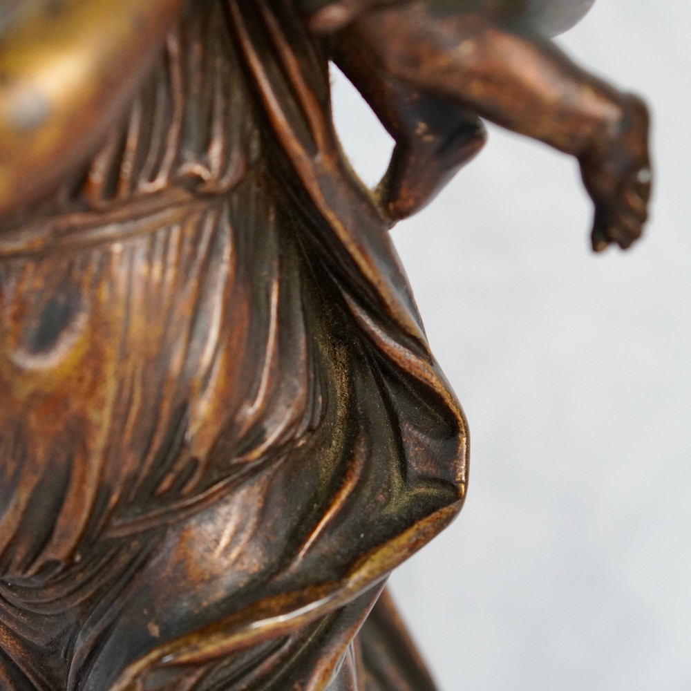 A patinated dark bronze sculpture depicting a draped classical woman holding a small child against her face, set upon a rounded bronze base. View III