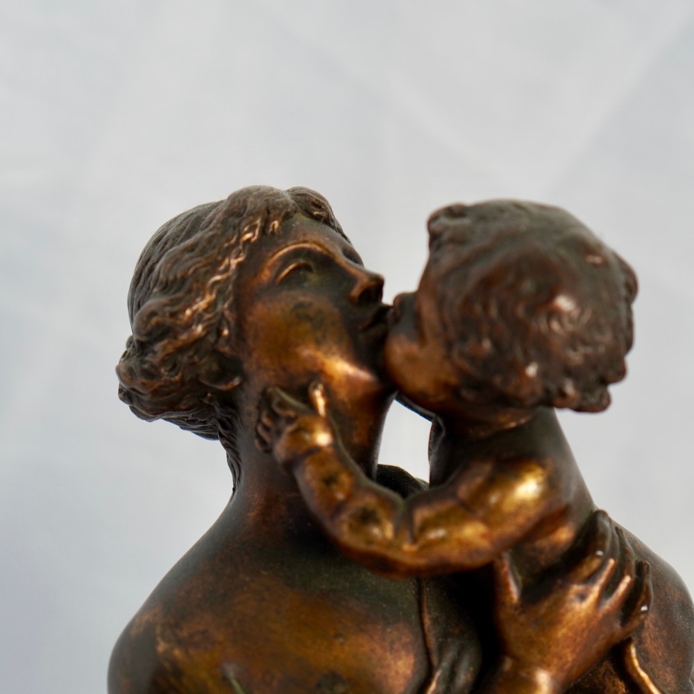 A patinated dark bronze sculpture depicting a draped classical woman holding a small child against her face, set upon a rounded bronze base. View IV