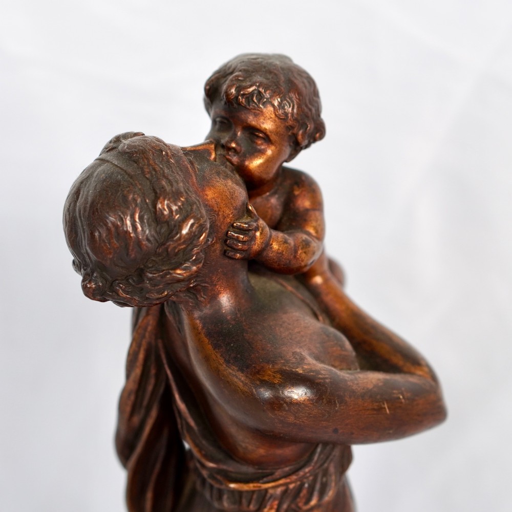 A patinated dark bronze sculpture depicting a draped classical woman holding a small child against her face, set upon a rounded bronze base. View V