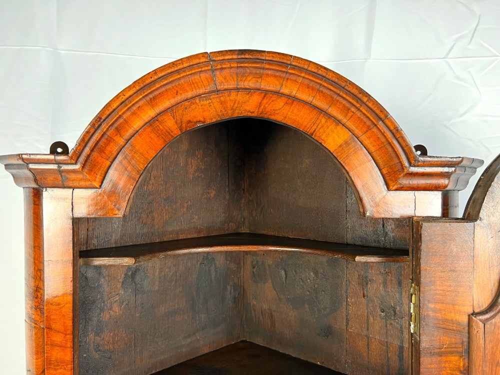 A Queen Anne walnut hanging corner cupboard featuring a double-moulded arched cornice, a mirrored door panel, and an integrated candle slide. View XIV