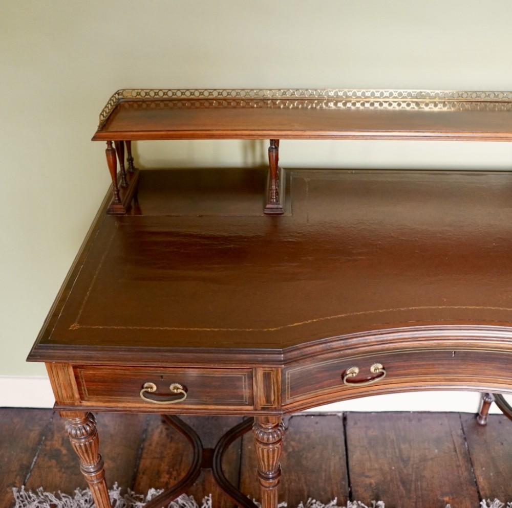 A Victorian rosewood writing desk featuring a brass gallery shelf, three drawers with brass handles, turned fluted legs, and curved stretchers. View II