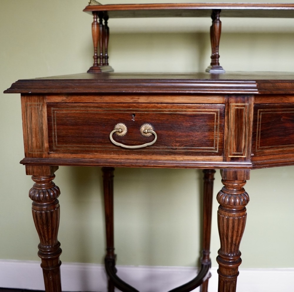 A Victorian rosewood writing desk featuring a brass gallery shelf, three drawers with brass handles, turned fluted legs, and curved stretchers. View IV
