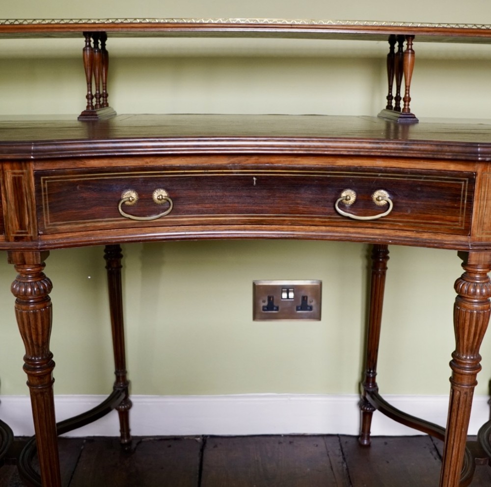 A Victorian rosewood writing desk featuring a brass gallery shelf, three drawers with brass handles, turned fluted legs, and curved stretchers. View V