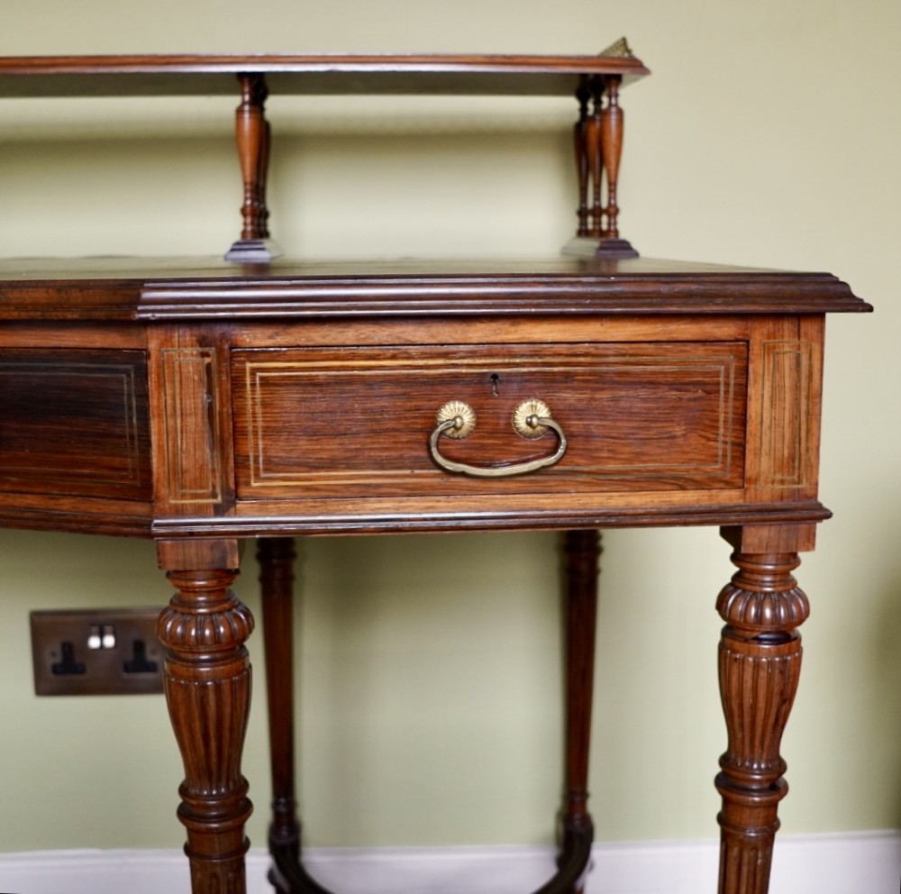 A Victorian rosewood writing desk featuring a brass gallery shelf, three drawers with brass handles, turned fluted legs, and curved stretchers. View VI