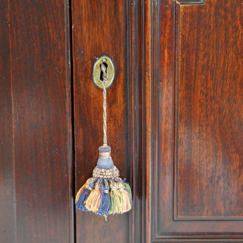 A Georgian mahogany hanging corner cupboard featuring an arched fielded panel door, brass H-hinges, key escutcheon, and a lower drawer. View III