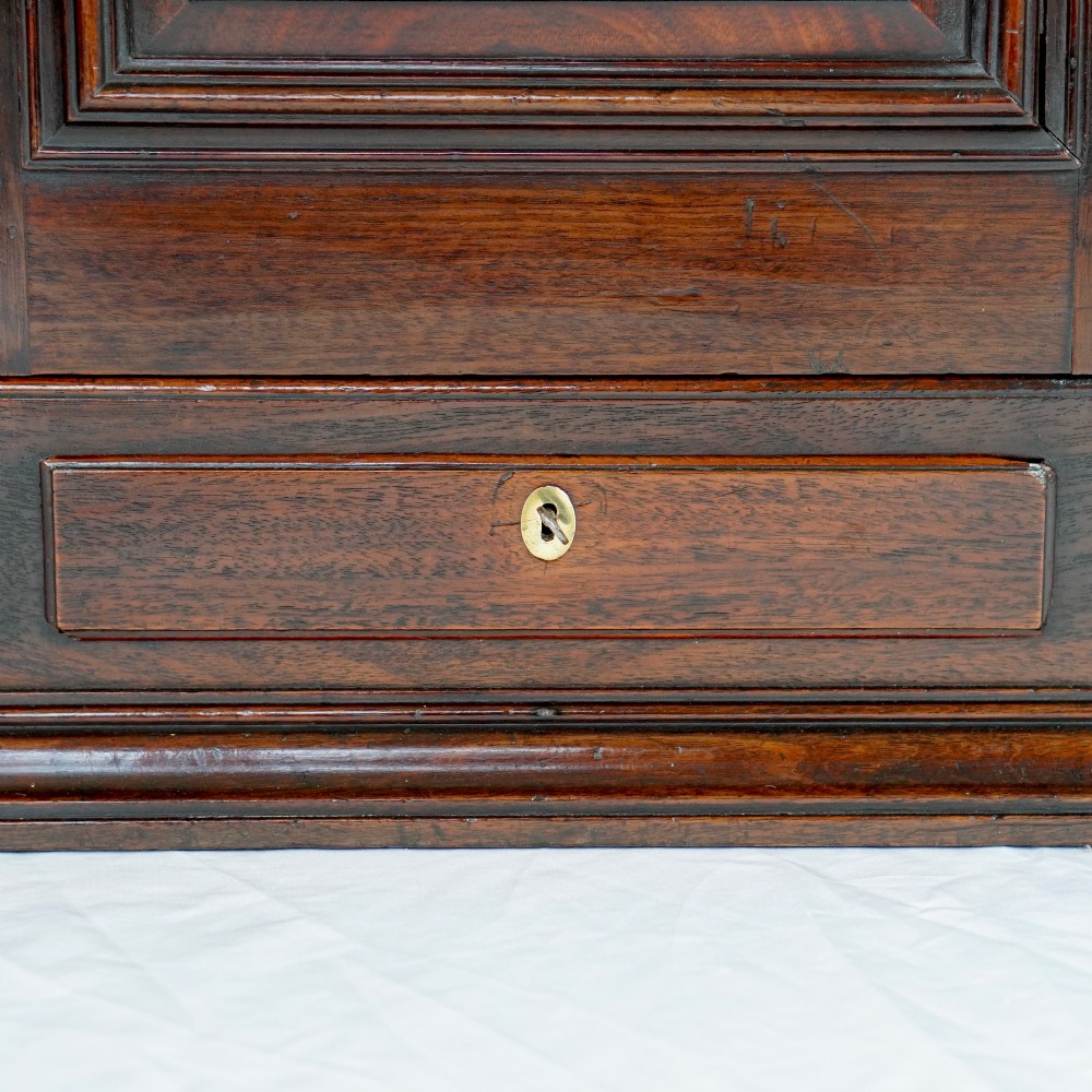 A Georgian mahogany hanging corner cupboard featuring an arched fielded panel door, brass H-hinges, key escutcheon, and a lower drawer. View V