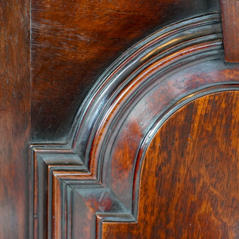 A Georgian mahogany hanging corner cupboard featuring an arched fielded panel door, brass H-hinges, key escutcheon, and a lower drawer. View VII