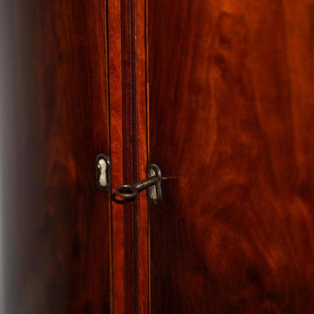 A George III bow front mahogany corner cabinet featuring polished plum pudding veneers, inlaid border stringing, and two curved doors. View V