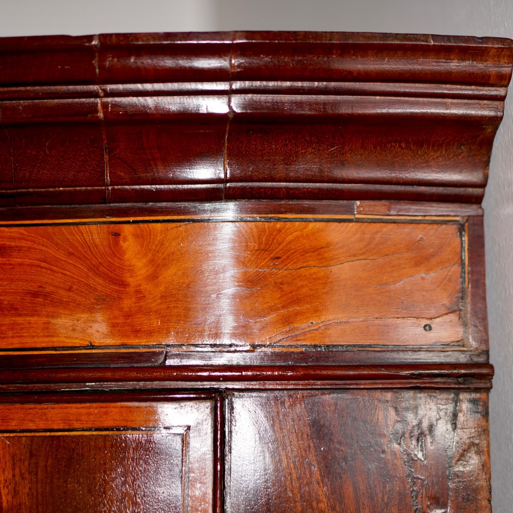 A George III bow front mahogany corner cabinet featuring polished plum pudding veneers, inlaid border stringing, and two curved doors. View VI