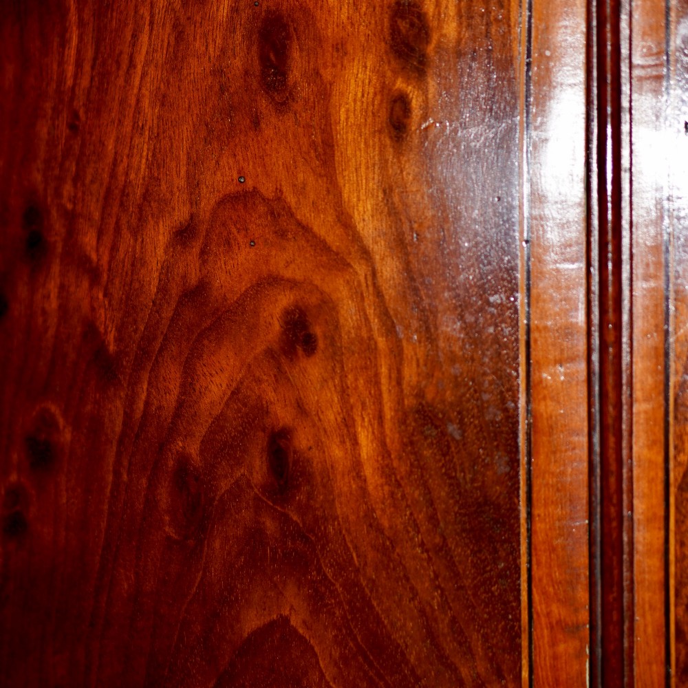 A George III bow front mahogany corner cabinet featuring polished plum pudding veneers, inlaid border stringing, and two curved doors. View VIII