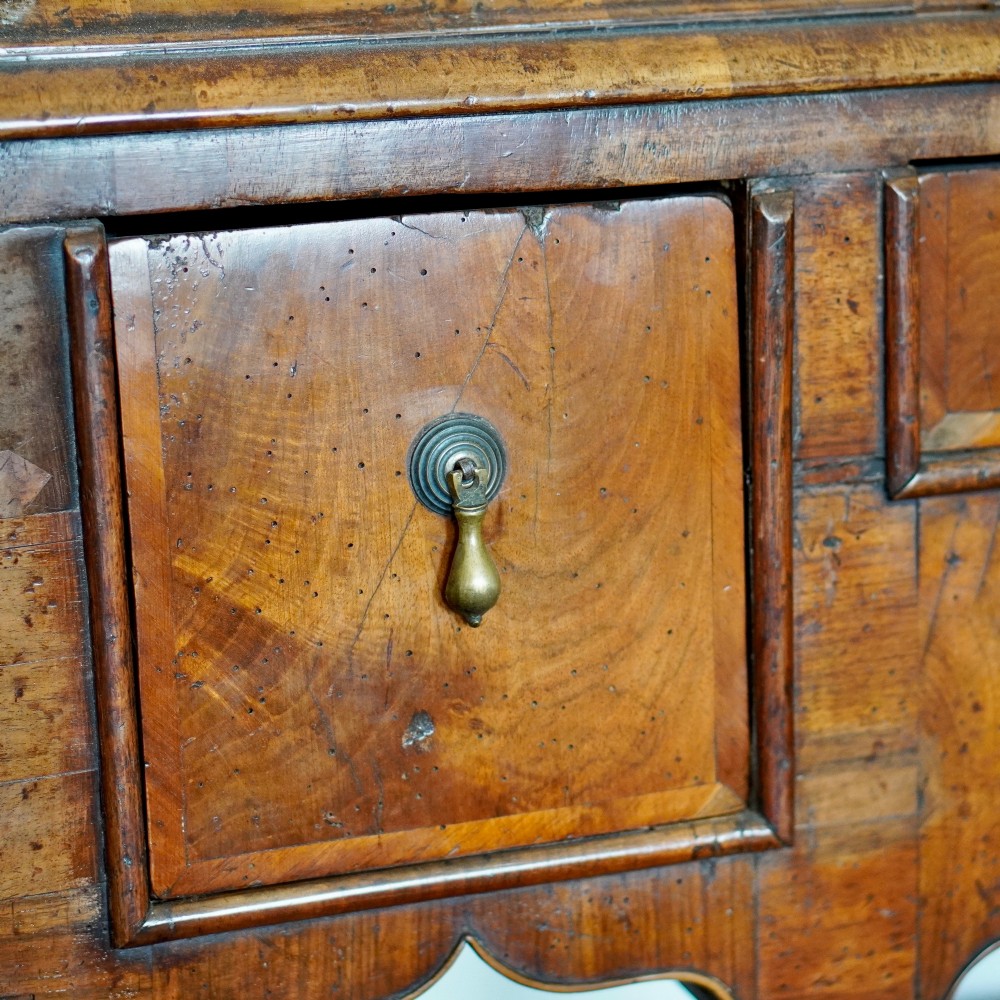 An early eighteenth-century Queen Anne walnut chest on stand featuring multiple drawers, brass teardrop handles, a shaped apron, and turned legs connected by stretchers. View VI