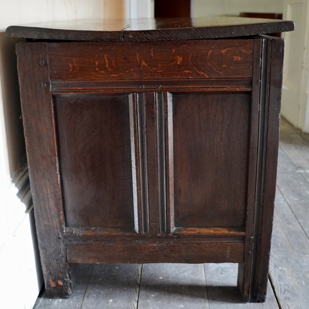 A 17th-century joined oak coffer featuring carved arch front panels, a carved top frieze, hinged lid, and brass keyhole escutcheon. View II