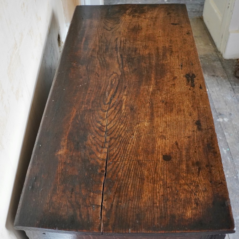 A 17th-century joined oak coffer featuring carved arch front panels, a carved top frieze, hinged lid, and brass keyhole escutcheon. View III