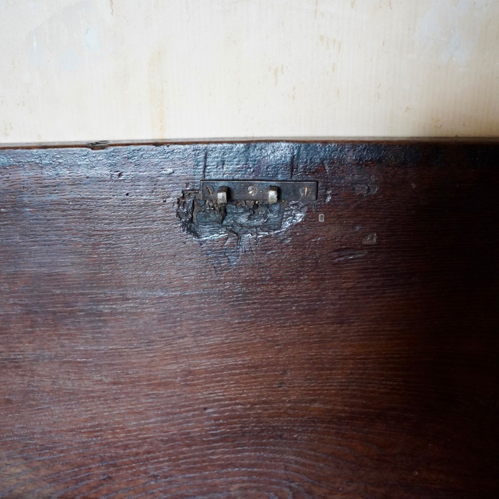 A 17th-century joined oak coffer featuring carved arch front panels, a carved top frieze, hinged lid, and brass keyhole escutcheon. View V