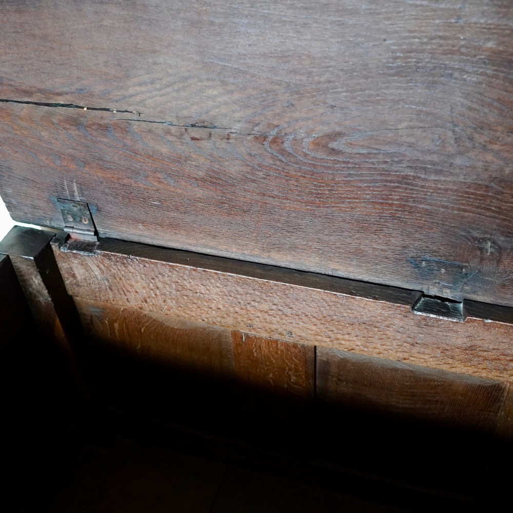 A 17th-century joined oak coffer featuring carved arch front panels, a carved top frieze, hinged lid, and brass keyhole escutcheon. View VII