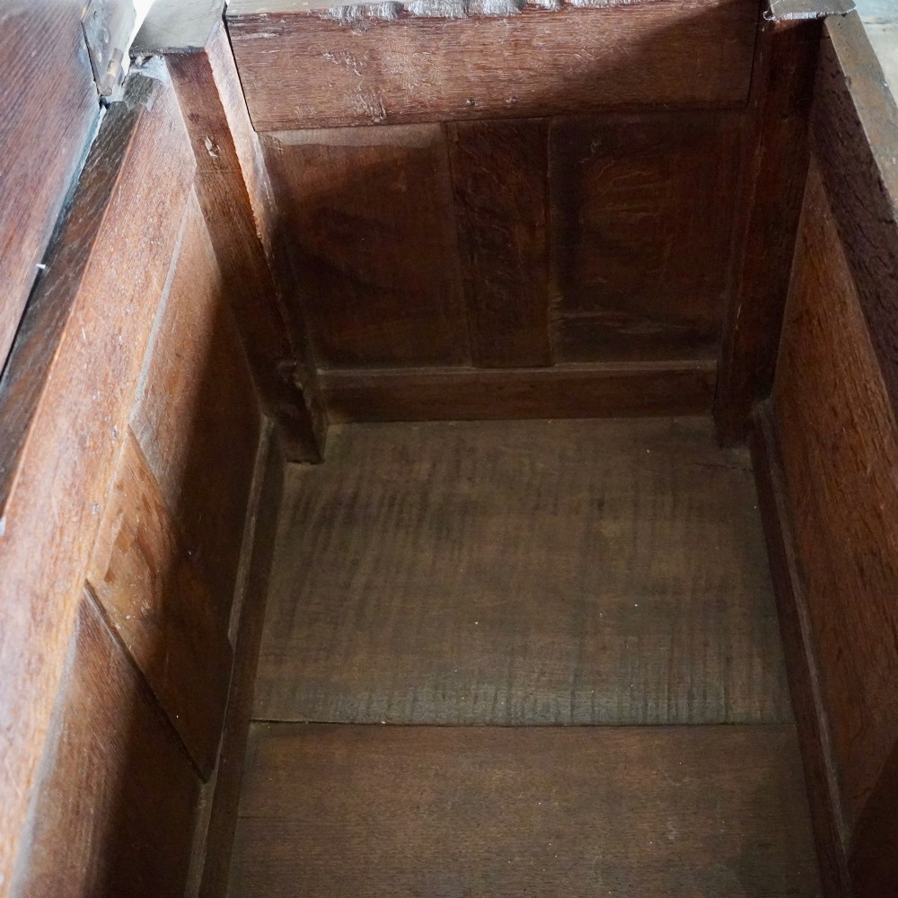 A 17th-century joined oak coffer featuring carved arch front panels, a carved top frieze, hinged lid, and brass keyhole escutcheon. View IX