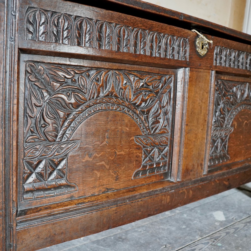 A 17th-century joined oak coffer featuring carved arch front panels, a carved top frieze, hinged lid, and brass keyhole escutcheon. View XI