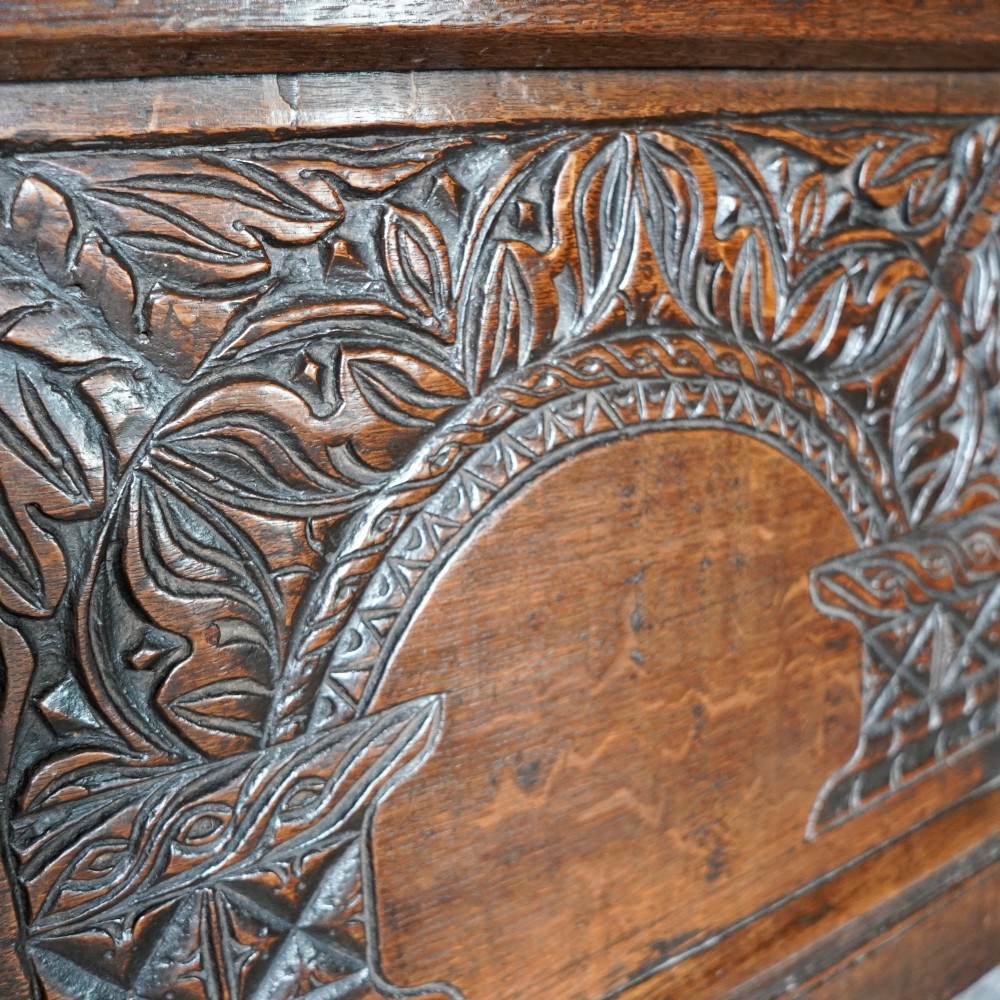 A 17th-century joined oak coffer featuring carved arch front panels, a carved top frieze, hinged lid, and brass keyhole escutcheon. View XII