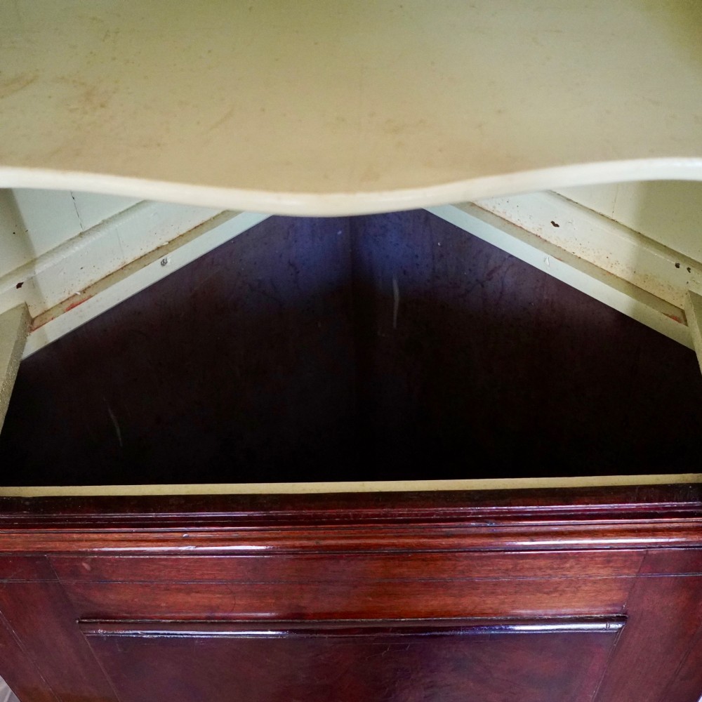 A tall George III standing mahogany corner cupboard featuring a swan-neck pediment with central brass finial and upper and lower fielded panel doors. View III