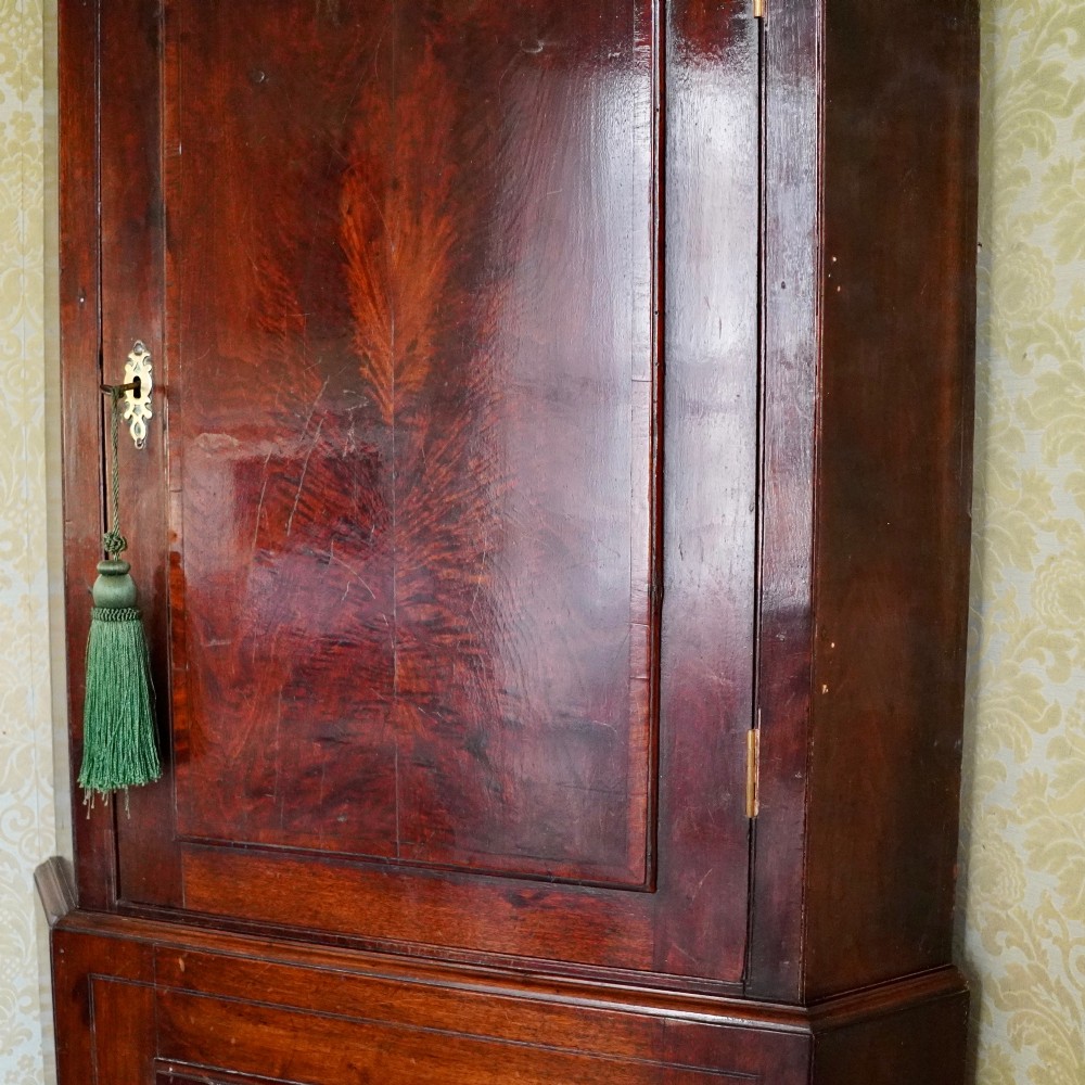 A tall George III standing mahogany corner cupboard featuring a swan-neck pediment with central brass finial and upper and lower fielded panel doors. View VII