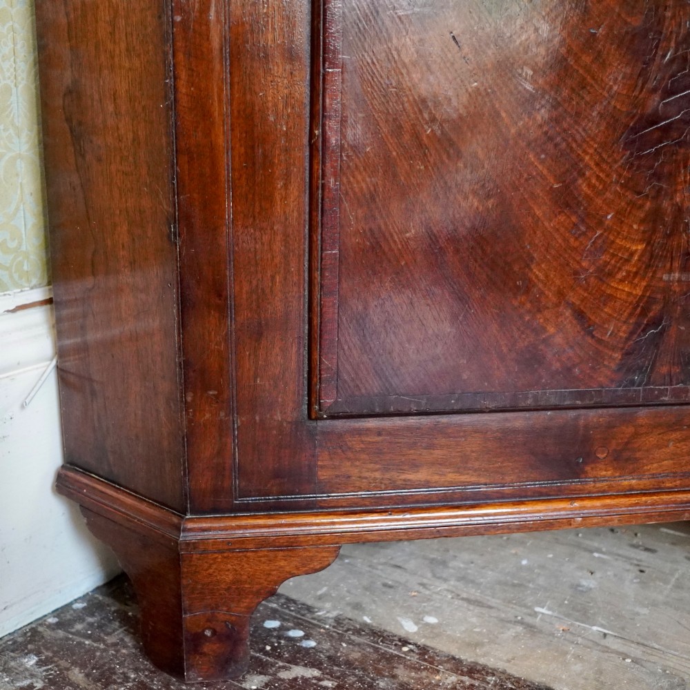 A tall George III standing mahogany corner cupboard featuring a swan-neck pediment with central brass finial and upper and lower fielded panel doors. View VIII