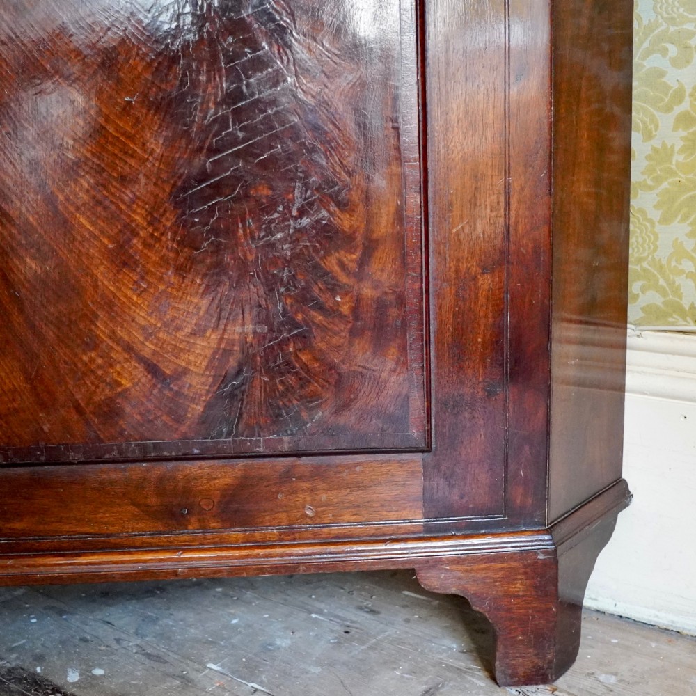 A tall George III standing mahogany corner cupboard featuring a swan-neck pediment with central brass finial and upper and lower fielded panel doors. View IX