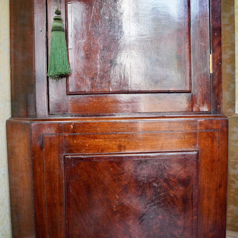 A tall George III standing mahogany corner cupboard featuring a swan-neck pediment with central brass finial and upper and lower fielded panel doors. View X