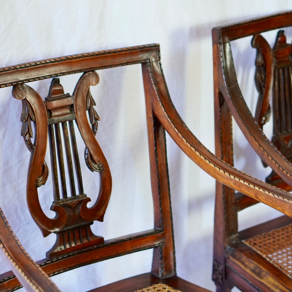 A matching pair of 19th-century Regency style mahogany armchairs featuring carved lyre back splats and woven cane seats. View V