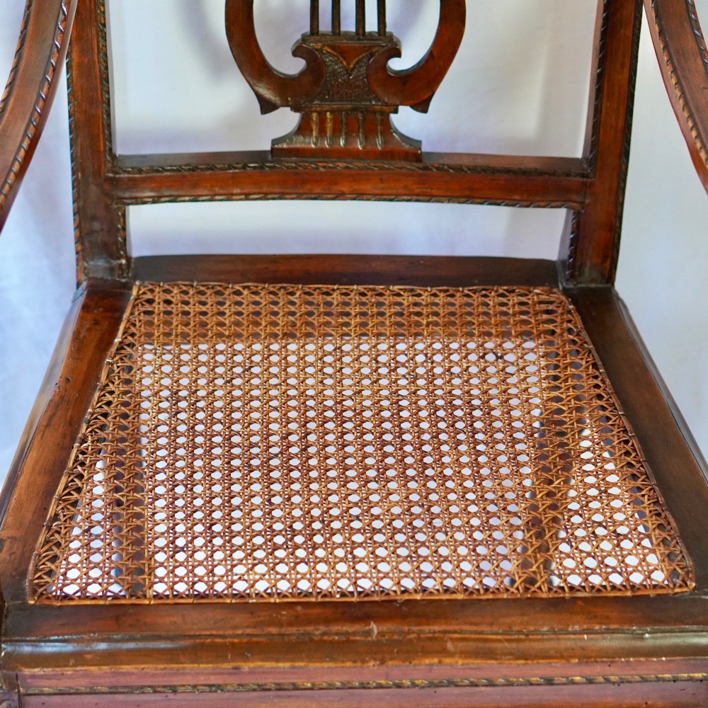 A matching pair of 19th-century Regency style mahogany armchairs featuring carved lyre back splats and woven cane seats. View X